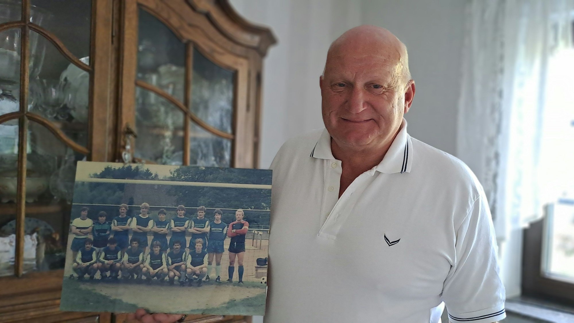 Ein Mann in weißem Shirt mit einem Mannschaftsfoto in der Hand.