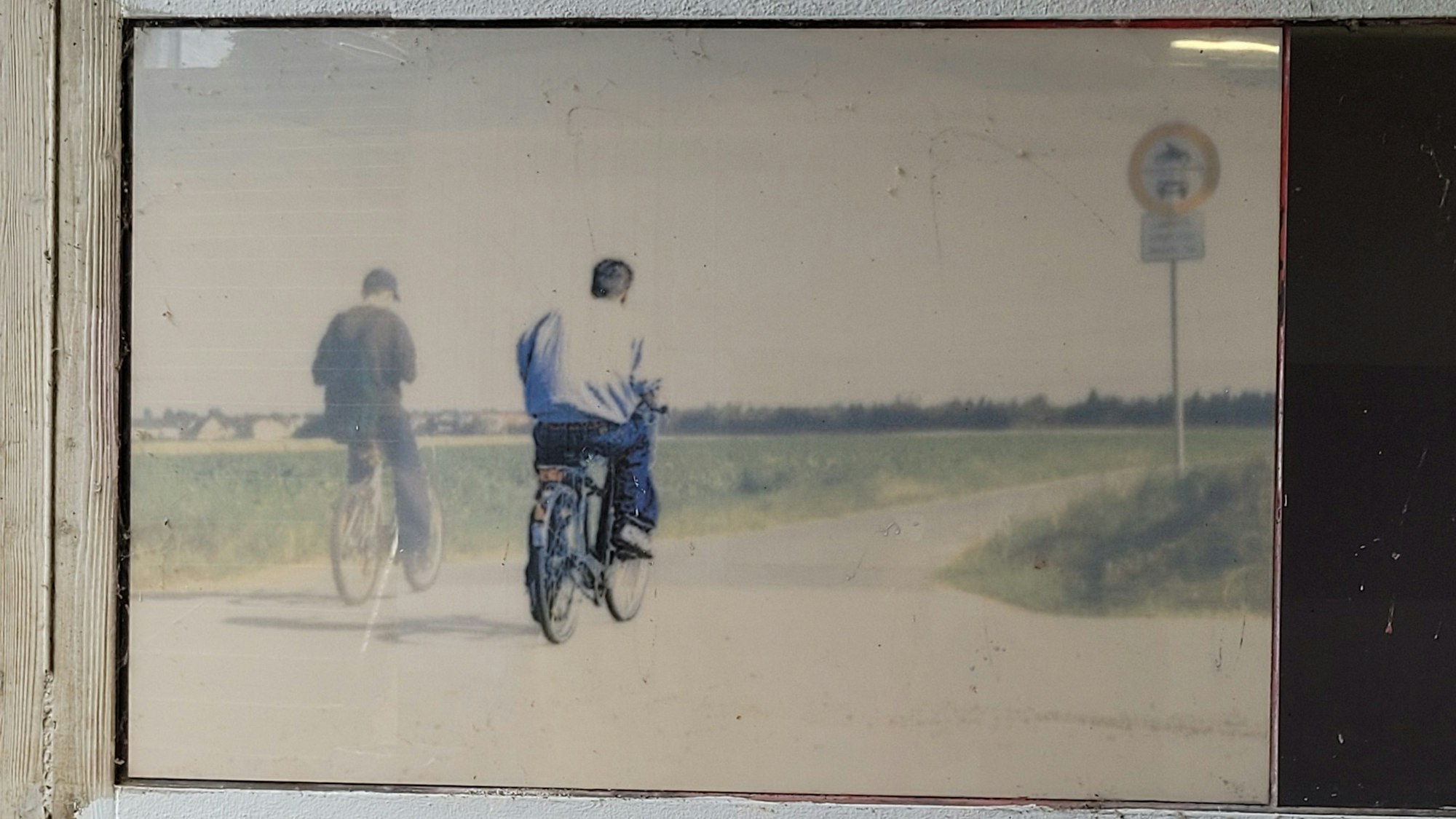 Zwei Männer auf Fahrrädern auf einem Weg zwischen Feldern.