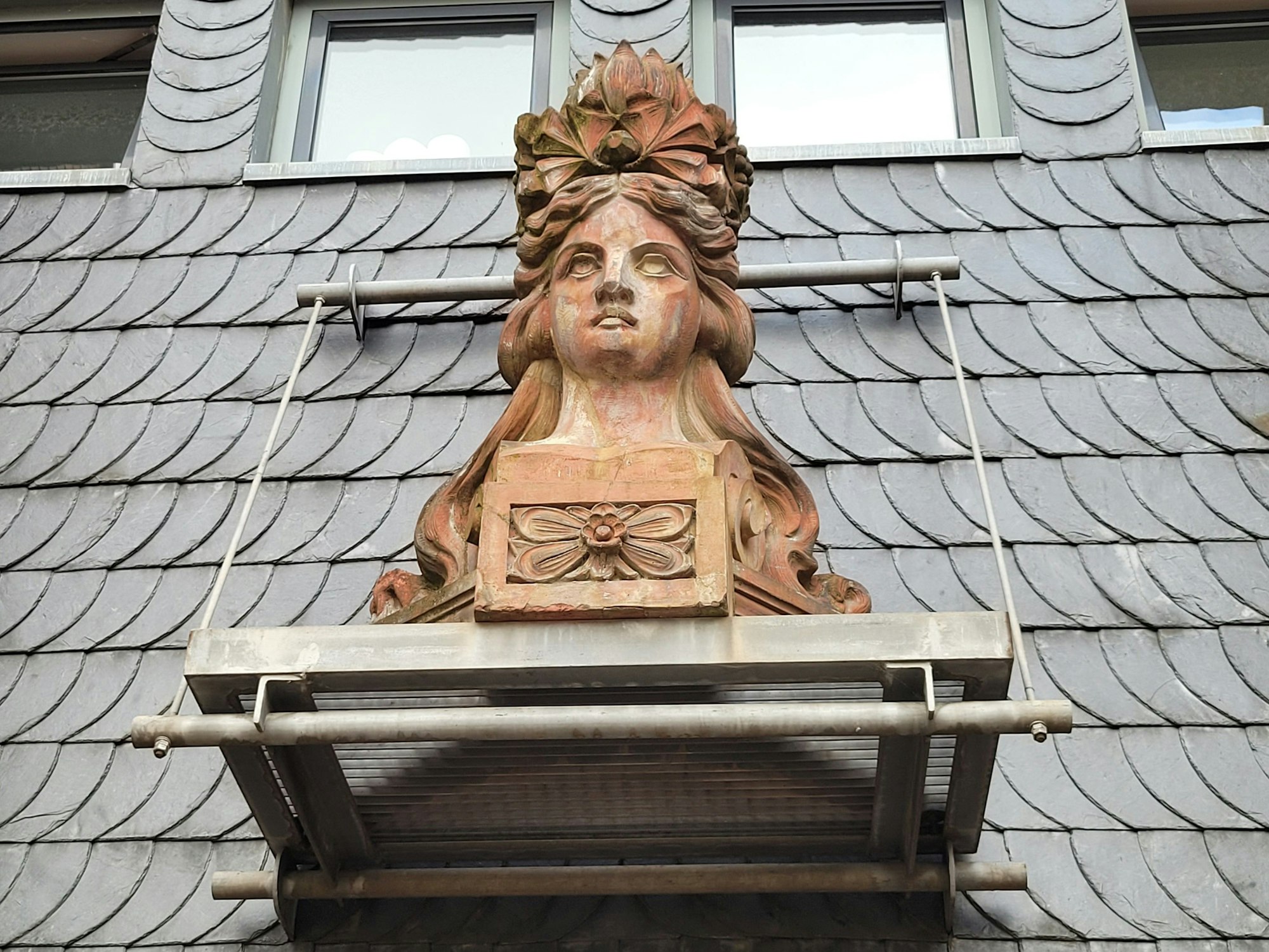 Eine Büste, sie zeigt eine Frau, sie hängt an einer Fassade.