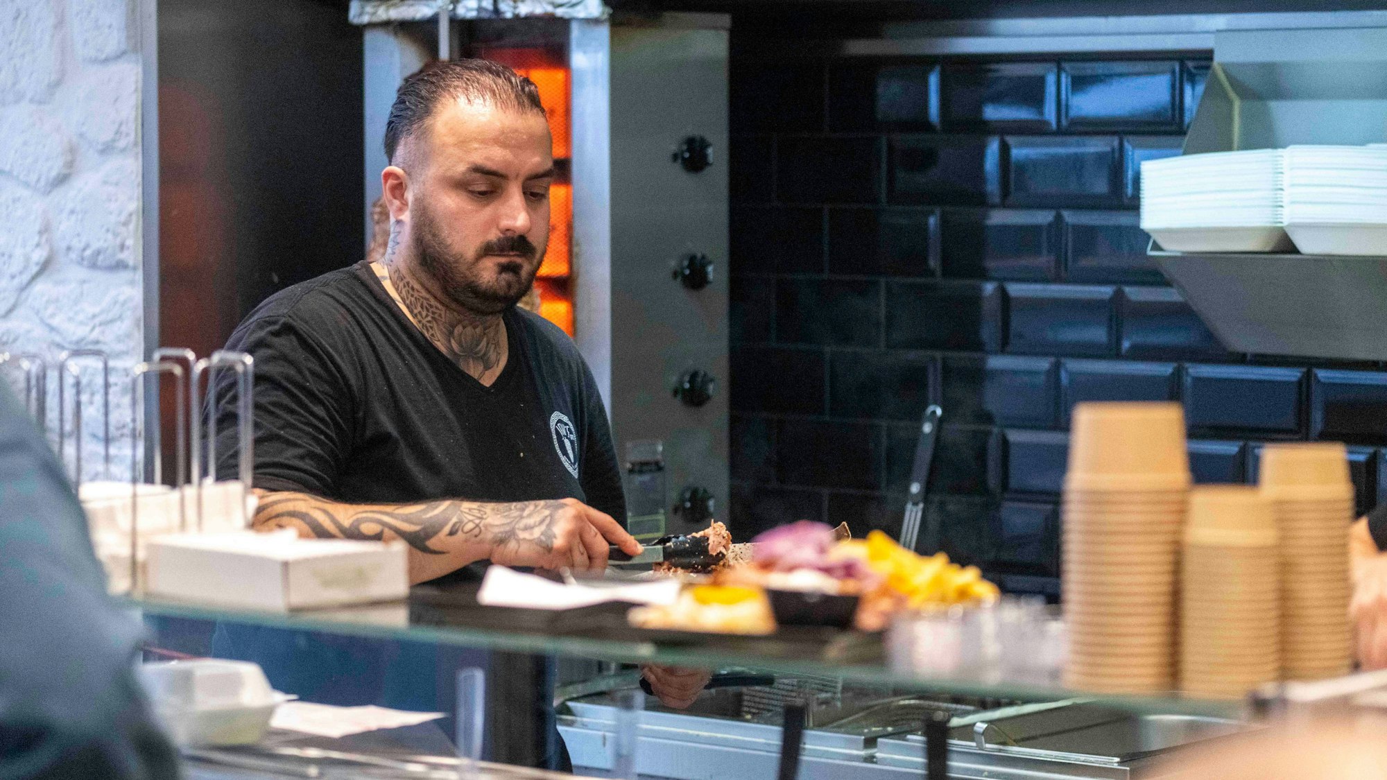 Das Bild zeigt den jungen Griechen, der gerade dabei ist, Gyros auf einen Teller zu verteilen.