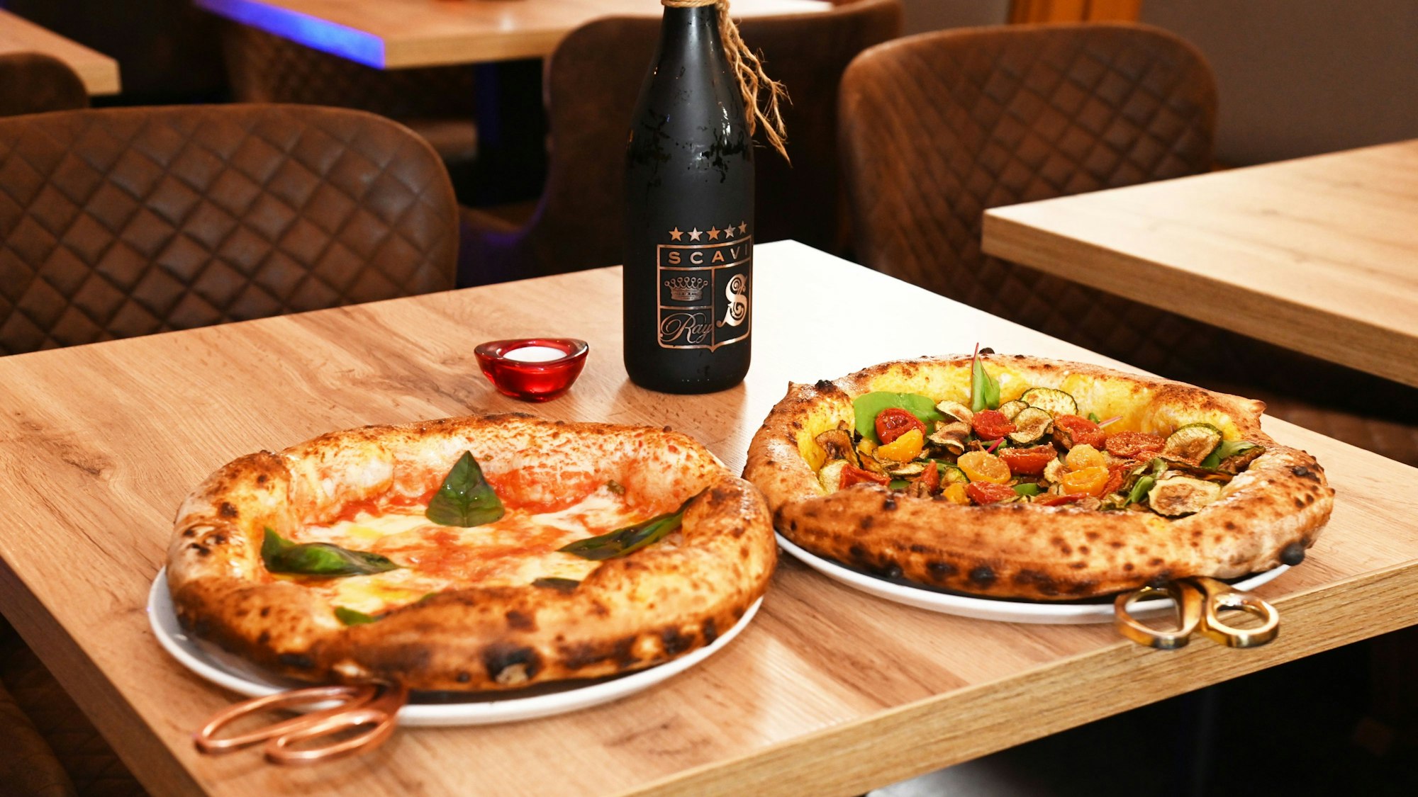 Zwei Pizzen mit dickem Rand stehen auf einem Tisch.