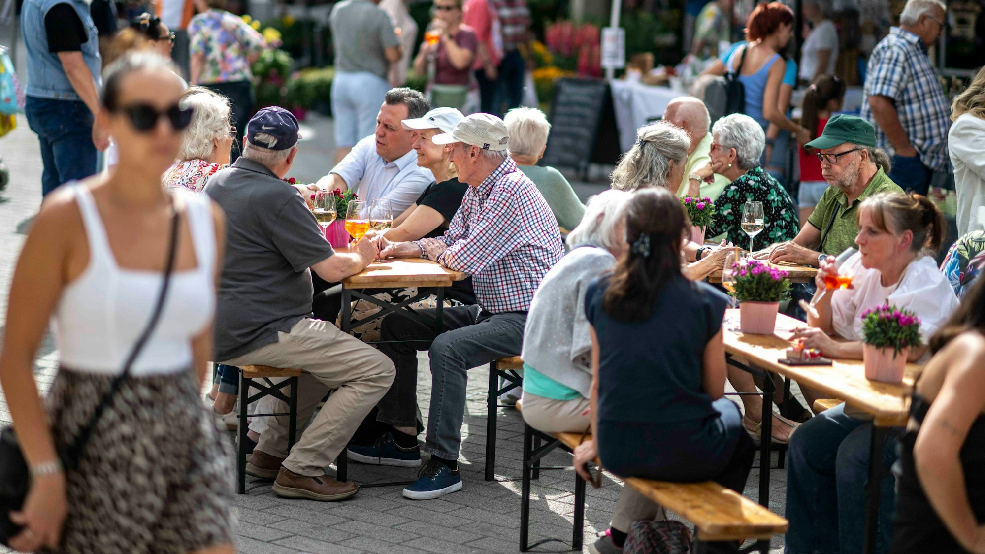 Das Bild zeigt den Euskirchener Feierabendmarkt. Einige Menschen sitzen auf Bierbänken und unterhalten sich.