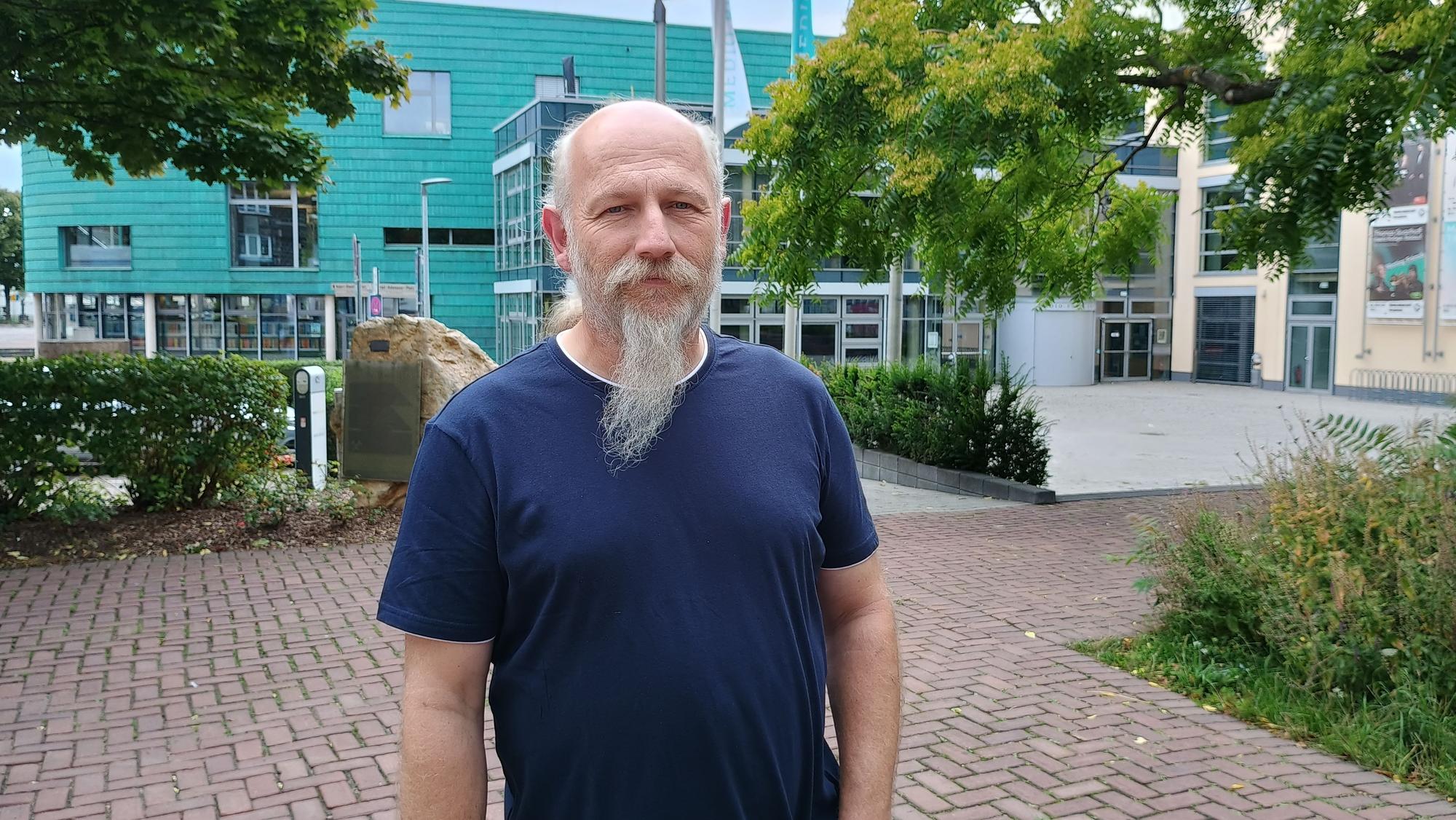 Peter Hirseler trägt ein dunkelblaues T-Shirt und hat einen Bart. Hinter ihm sieht man einige Bäume und das Medio Rhein Erft.