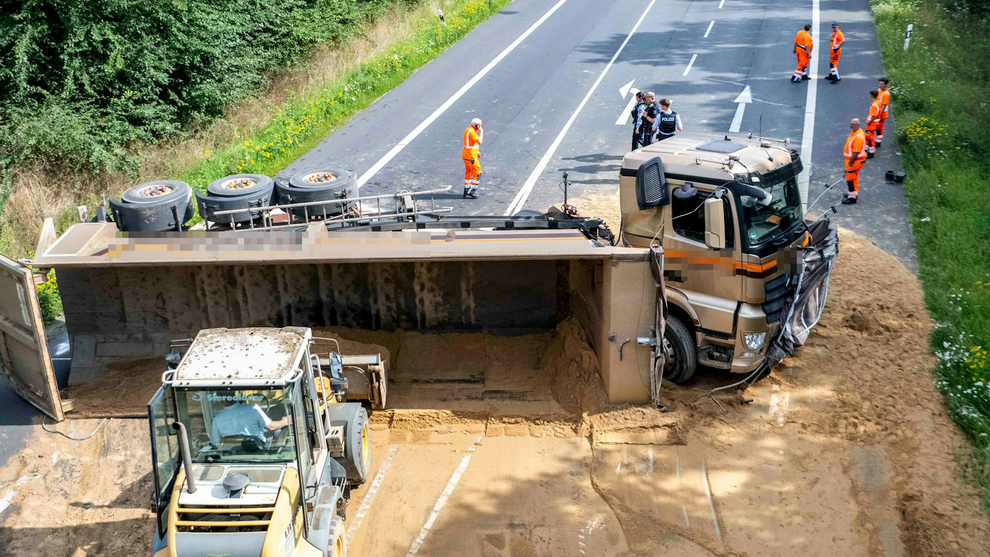 Der Auflieger eines Lkw ist umgekippt und Sand liegt auf der Straße. Das Bild zeigt die Aufräumarbeiten nach dem Unfall.