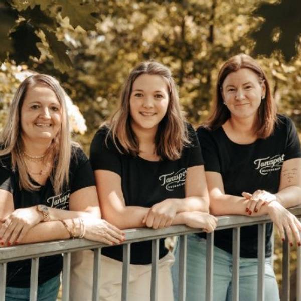 Drei Frauen lehnen lässig auf einem Geländer und tragen dabei das gleiche T-Shirt.