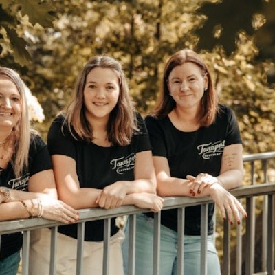 Drei Frauen lehnen lässig auf einem Geländer und tragen dabei das gleiche T-Shirt.