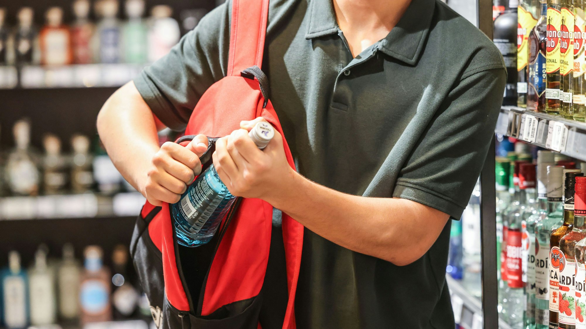 Ein Mann steckt in einem Supermarkt eine Flasche mit einem alkoholhaltigen Getränk in seinen Rucksack. (Symbolbild)