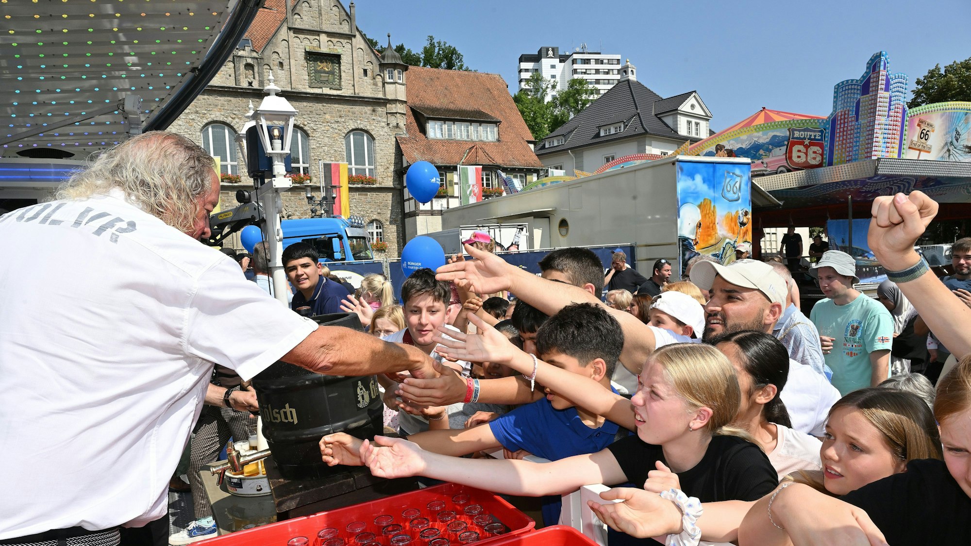 Ein Mann verteilt vor dem Rathaus in Bergisch Gladbach Freifahrchips an Kinder und Jugendliche. Die strecken erwartungsvoll die Hände aus.