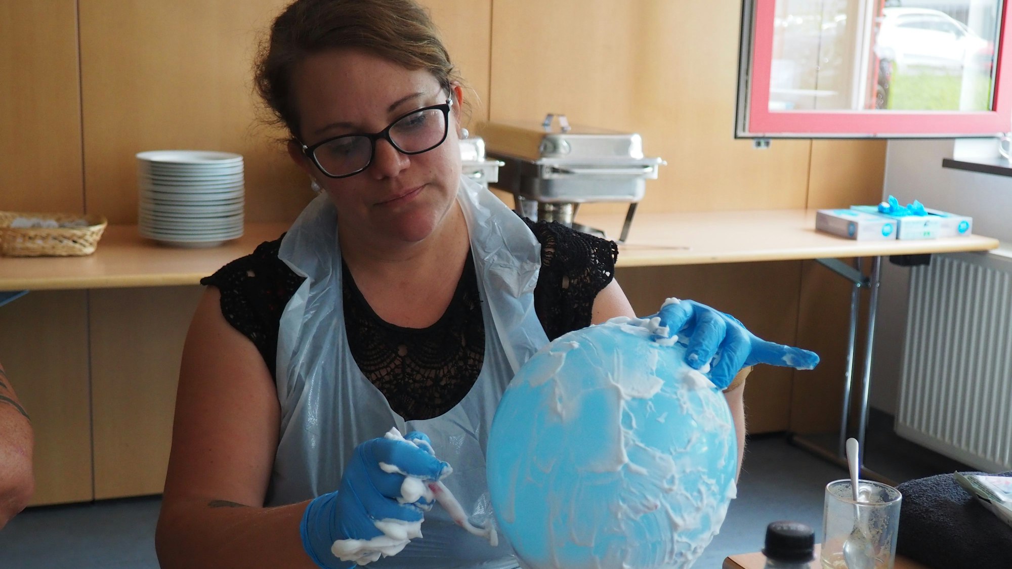 Hanna hat Rasierschaum auf einem blauen Luftballon aufgetragen und zieht behutsam einen Nassrasierer darüber.