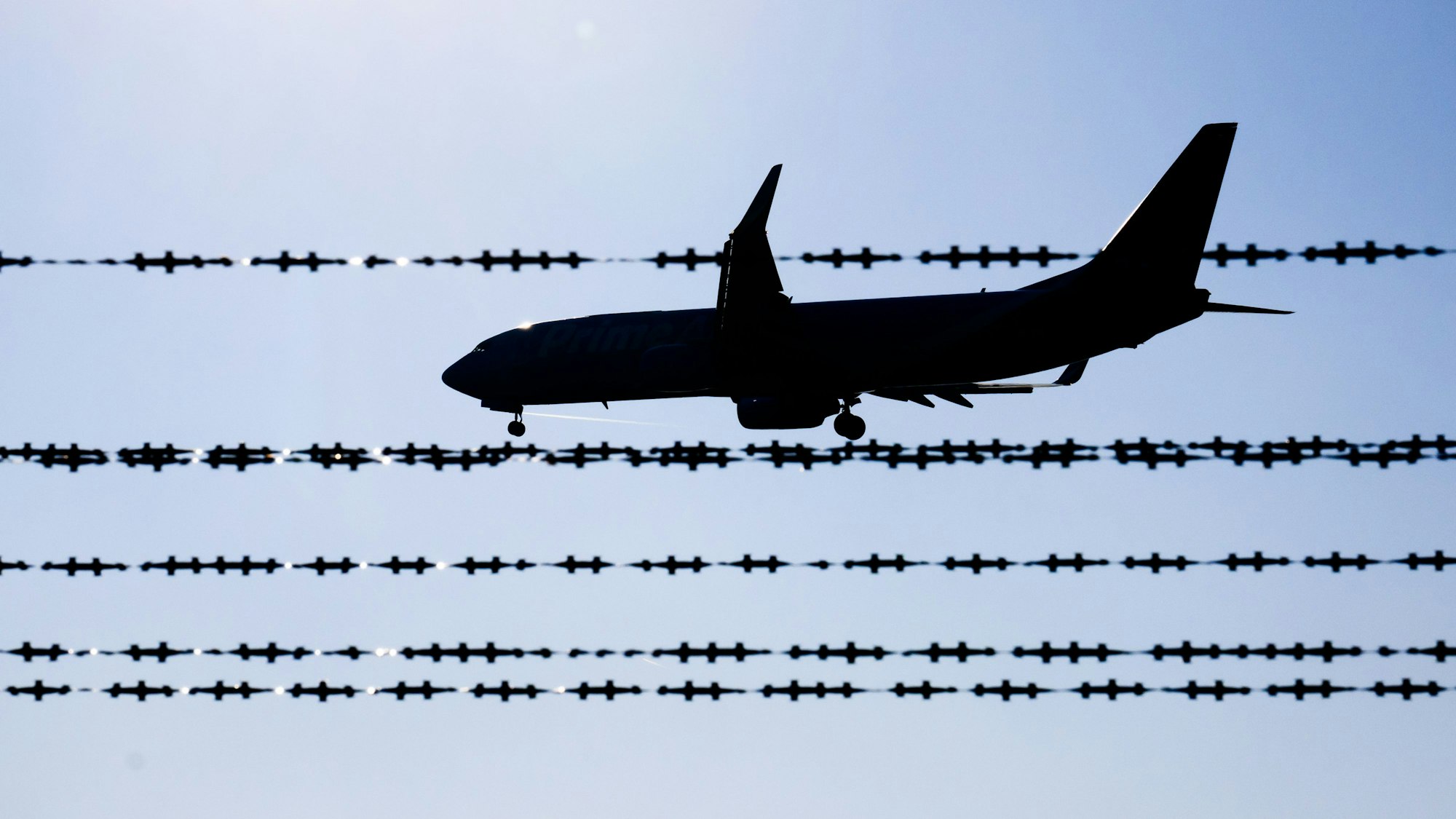 ARCHIV - 17.02.2025, Niedersachsen, Langenhagen: Ein Flugzeug fliegt hinter Stacheldraht am Flughafen Hannover. (zu dpa: «Landkreis weist Kritik an Abschiebung zurück») Foto: Julian Stratenschulte/dpa +++ dpa-Bildfunk +++