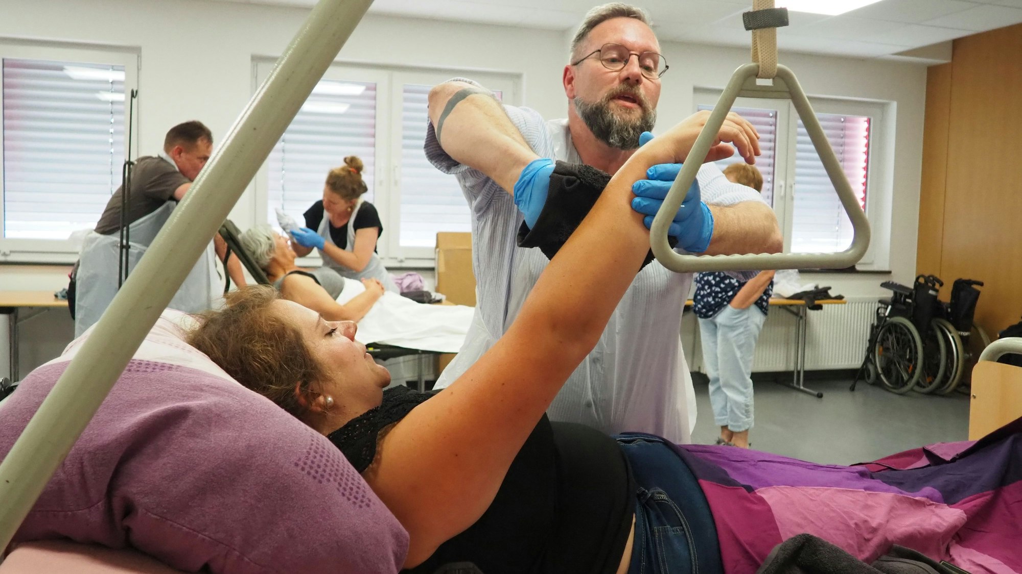 Eine Kursteilnehmerin streckt im Bett liegend ihren Arm hoch, damit Georg in mit einem Waschlappen säubern kann.