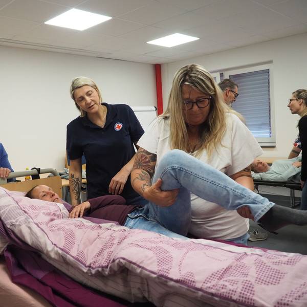 Eine Teilnehmerin schaut zu, wie Tanja eine Kursteilnehmerin im Pflegebett umlagert. Simone Pesch gibt dazu Hinweise.