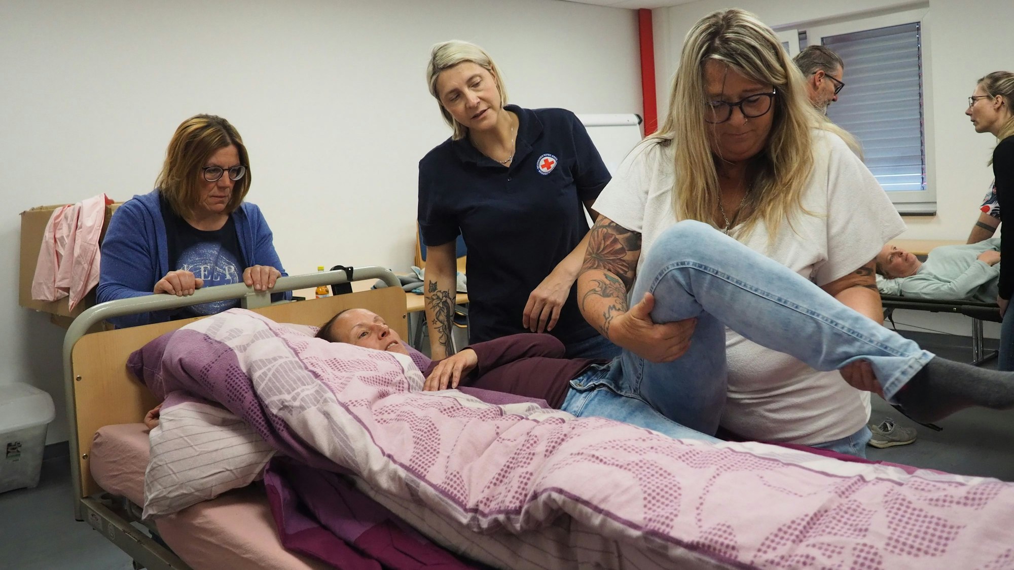 Eine Teilnehmerin schaut zu, wie Tanja eine Kursteilnehmerin im Pflegebett umlagert. Simone Pesch gibt dazu Hinweise.
