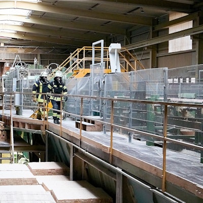 Zwei Feuerwehrmänner unter Atemschutz gehen durch eine der Produktionshallen.