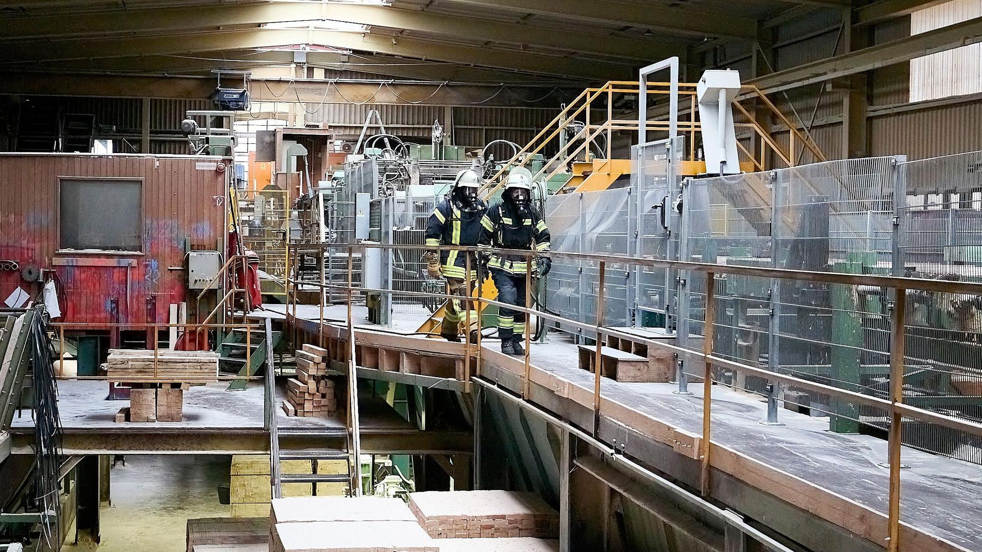 Zwei Feuerwehrmänner unter Atemschutz gehen durch eine der Produktionshallen.