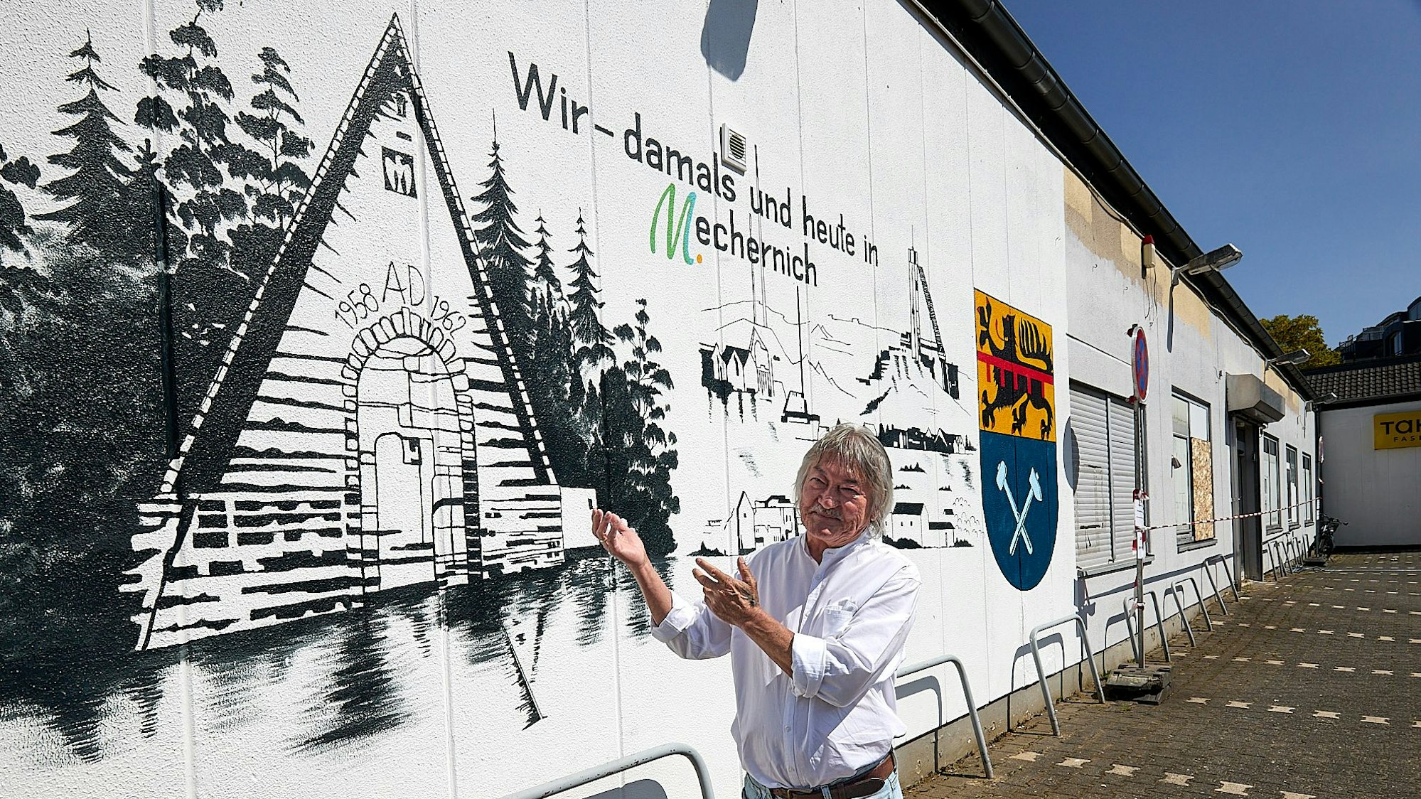 Yklas Kozikejew steht vor seinem Bild auf der Wand eines Gebäudes und zeigt darauf.