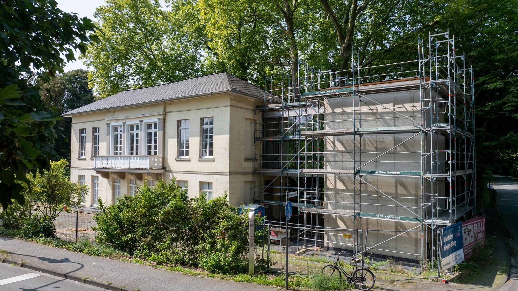 Der denkmalgeschützte Bahnhof Belvedere in Köln Müngersdorf ist von Bäumen umgeben. Ein Gebäudeteil ist eingerüstet.