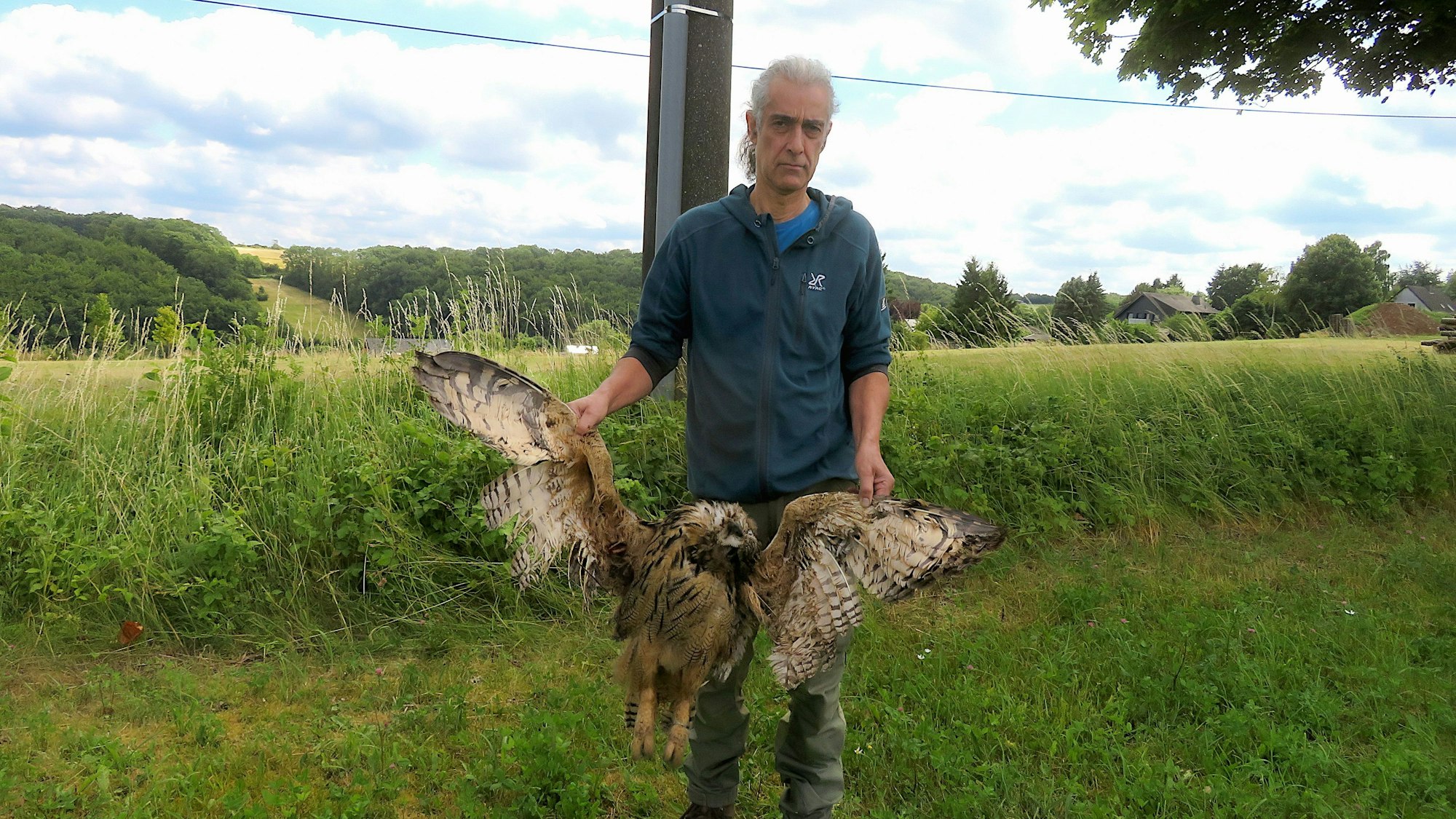 Stefan Brücher steht mit einem toten Uhu unter einem Strommast.