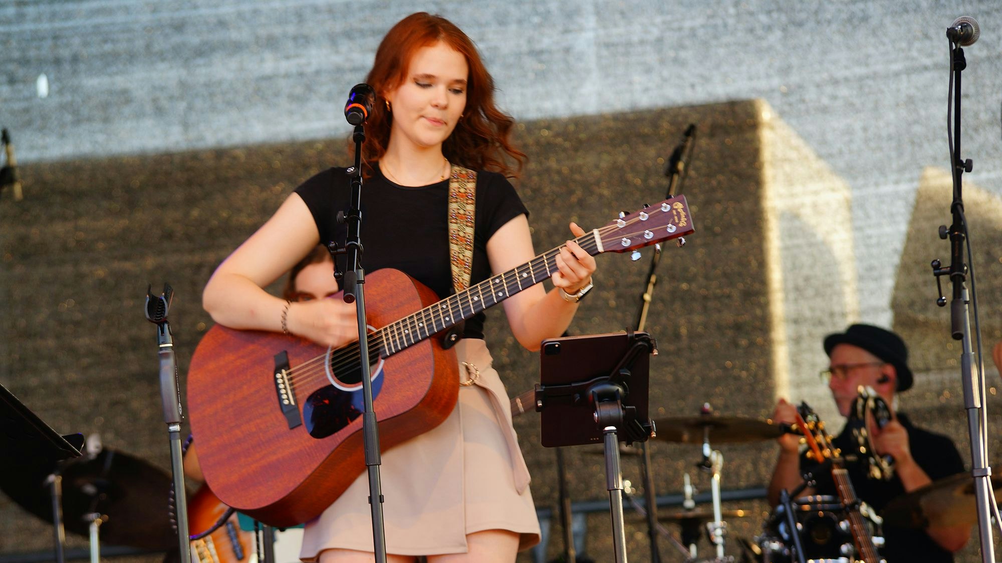 Zu sehen istg eine junge Musikerin mit Gitarre an einem Mikrofon.