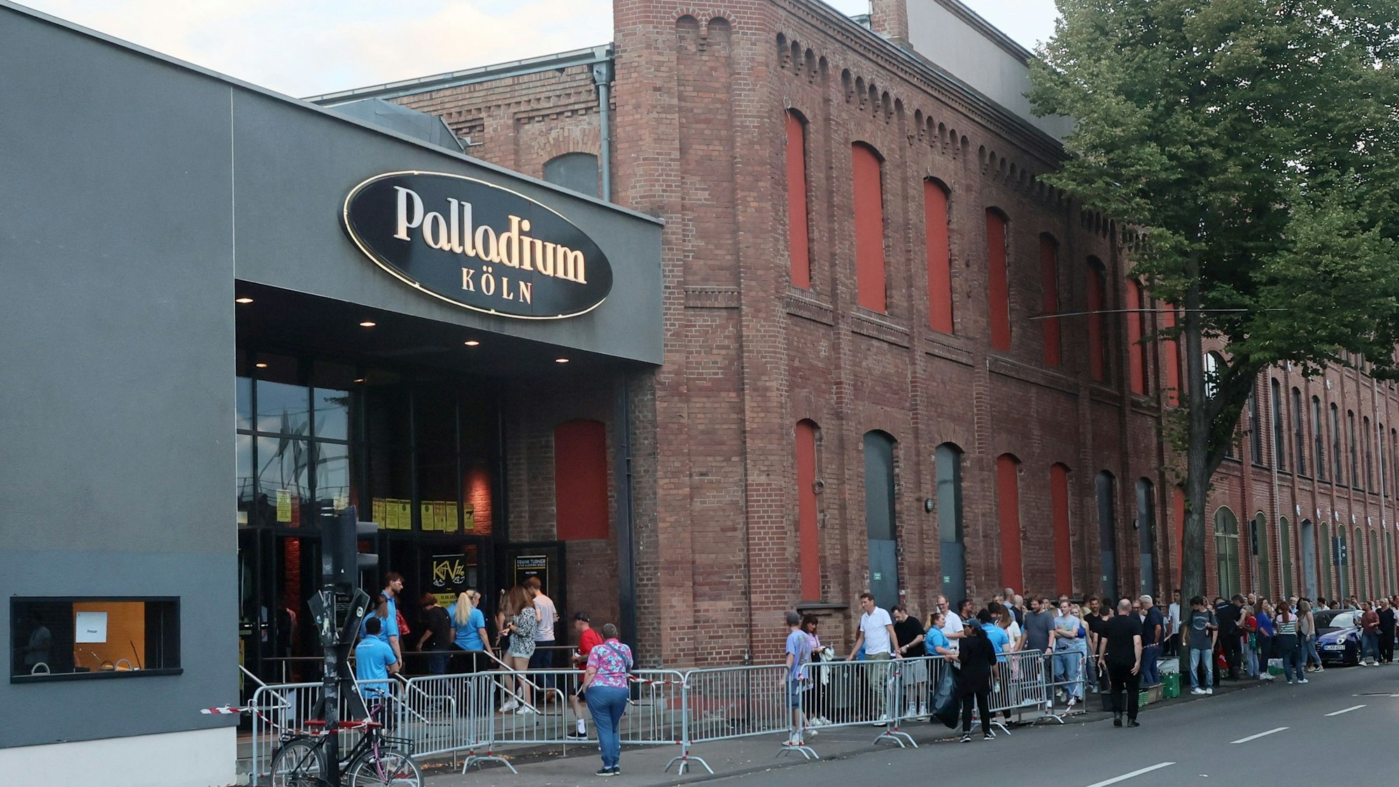 Vor einem Backsteingebäude mit großem Eingang hat sich eine Schlange gebildet.