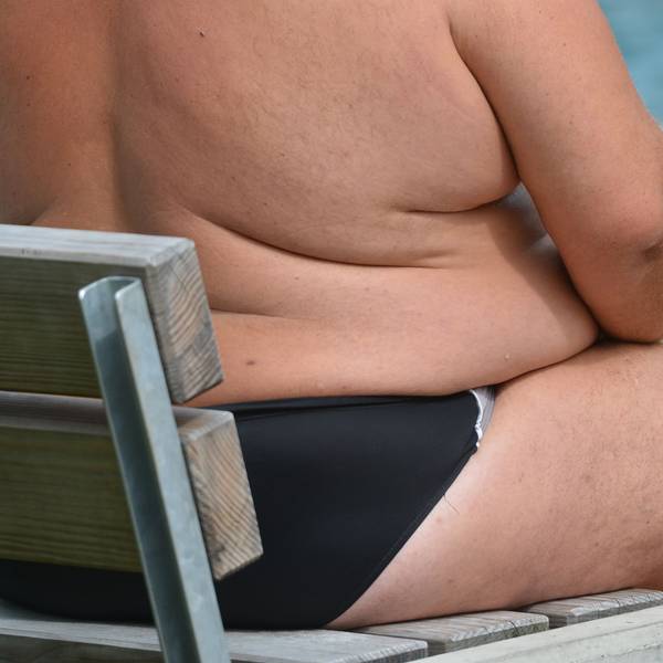 Ein übergewichtiger Mann sitzt in einem Freibad.