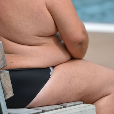 Ein übergewichtiger Mann sitzt in einem Freibad.