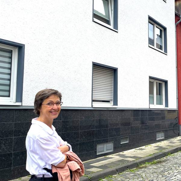 Eine Frau schaut in die Kamera, während sie durch eine schmale Straße geht.