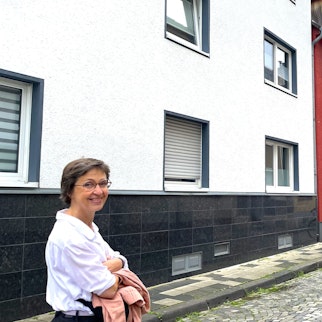 Eine Frau schaut in die Kamera, während sie durch eine schmale Straße geht.