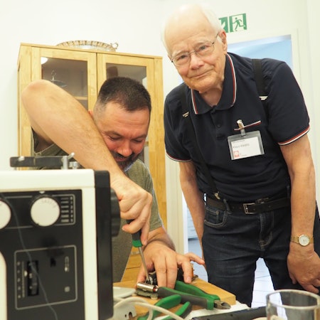 Das Bild zeigt zwei Männer, einer schraubt, der andere schaut in die Kamera.