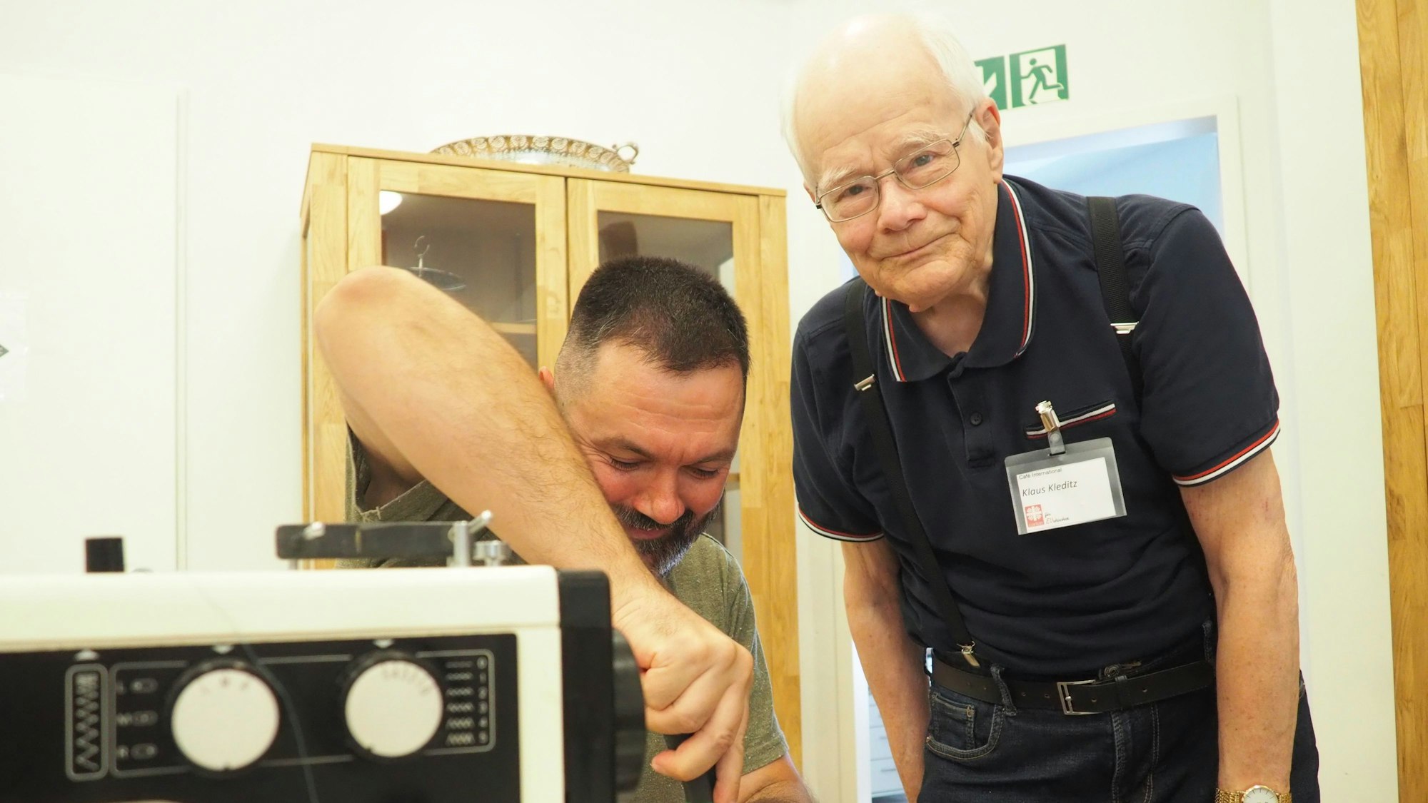 Das Bild zeigt zwei Männer, einer schraubt, der andere schaut in die Kamera.