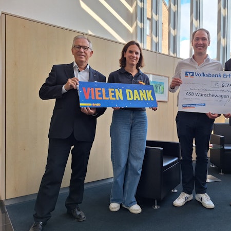 Eine Frau und drei Männer lächeln in die Kamera, zwei der Männer halten einen symbolischen Scheck über 6.750 Euro in den Händen.