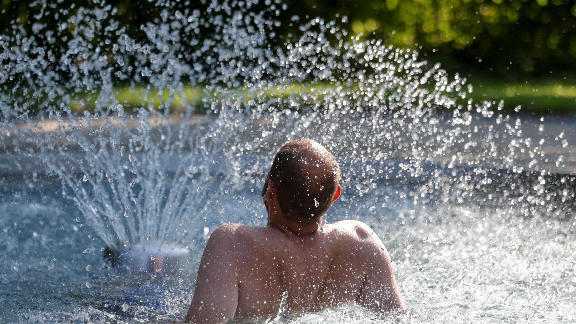 Das Bild zeigt einen Mann, der sich im Freibad an einem Wasserspiel erfrischt. Foto: Thomas Warnack/dpa