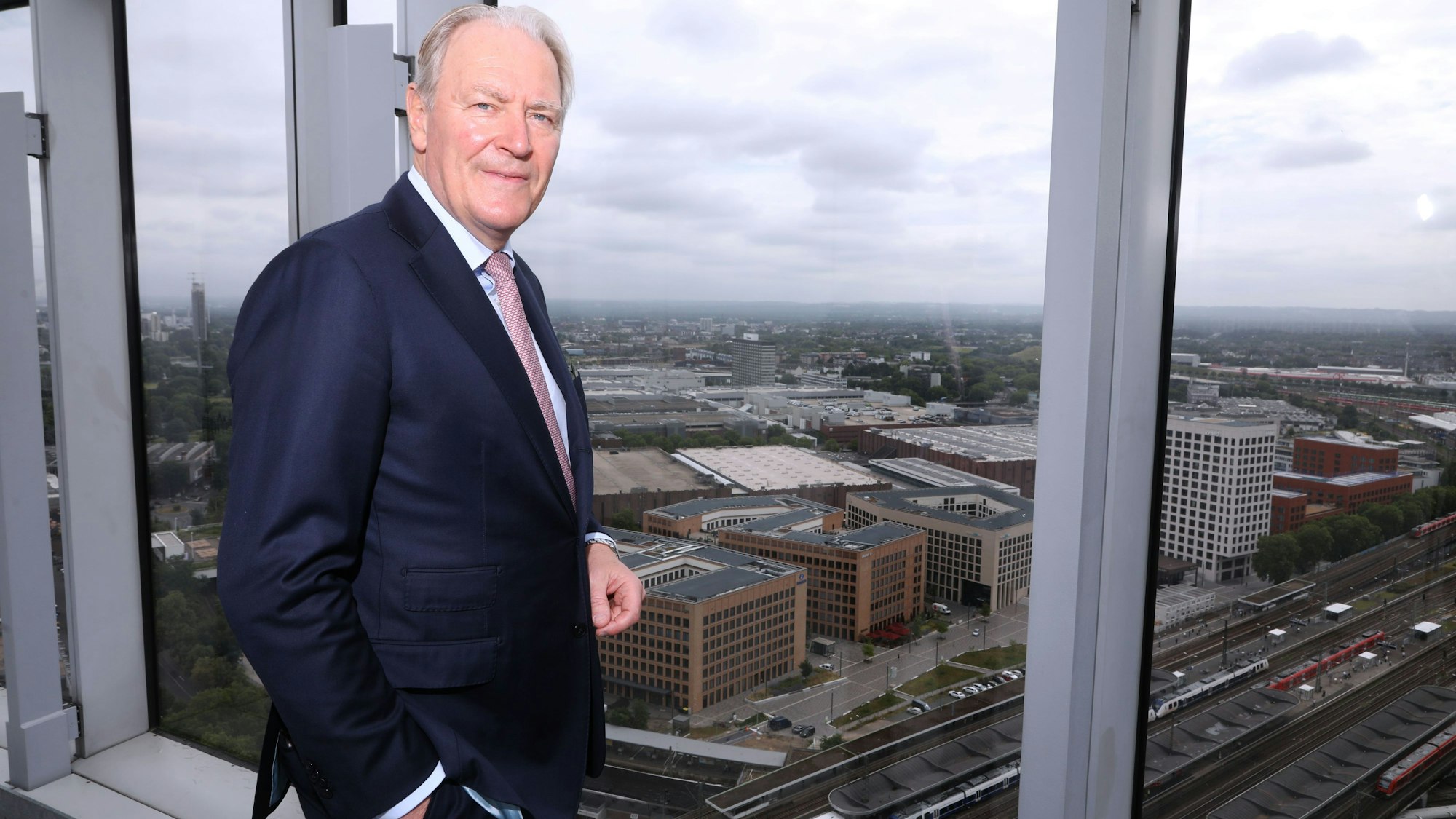 Gerald Böse, Vorsitzender der Geschäftsführung der Kölnmesse, steht an einem Fenster hoch über den Messehallen.