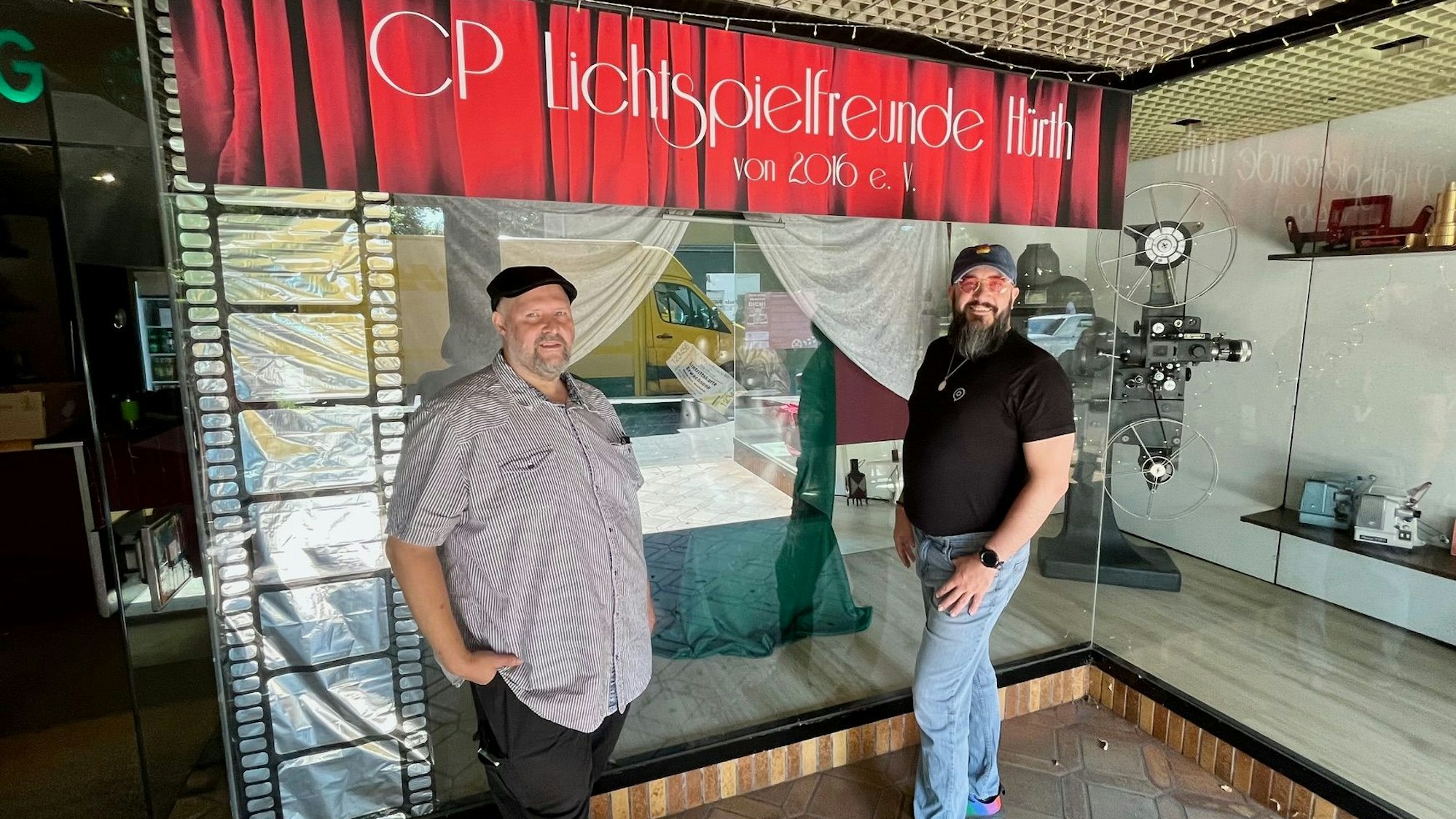 Die beiden Männer stehen vor einer Glasscheibe, darüber die Aufschrift: CP Lichtspielfreunde Hürth.