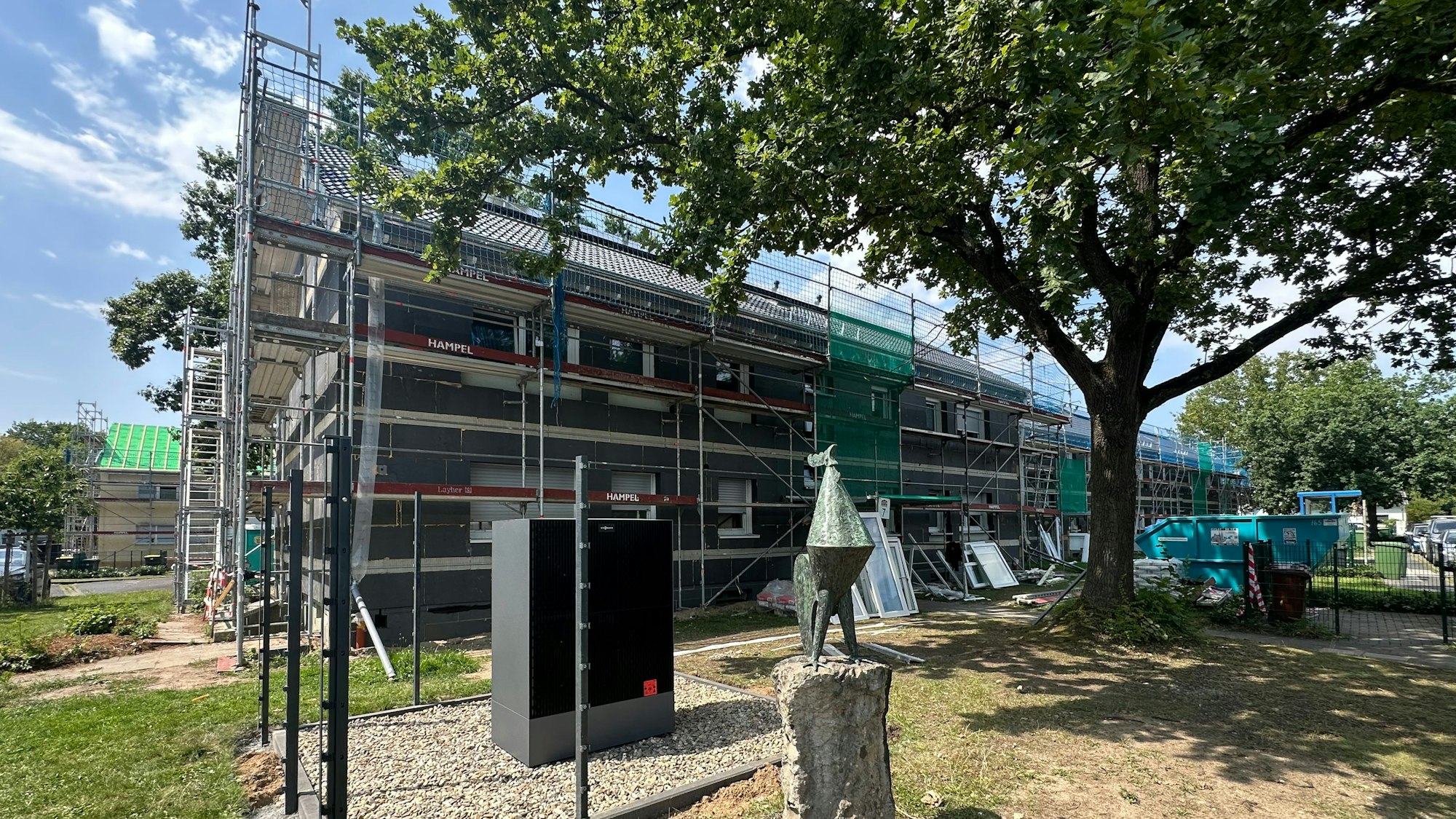 „Eingerüstet und schon isoliert sind die einige Häuser in der Berliner Straße. Vor Haus Nummer 7 steht der von Karl-Heinz Felinger gestaltete Hahn, der die Wärmepumpen „bewacht“.