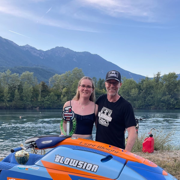 Eine junge Frau steht mit ihrem Vater hinter einem Jet-Ski und präsentiert ihren gewonnen Pokal.