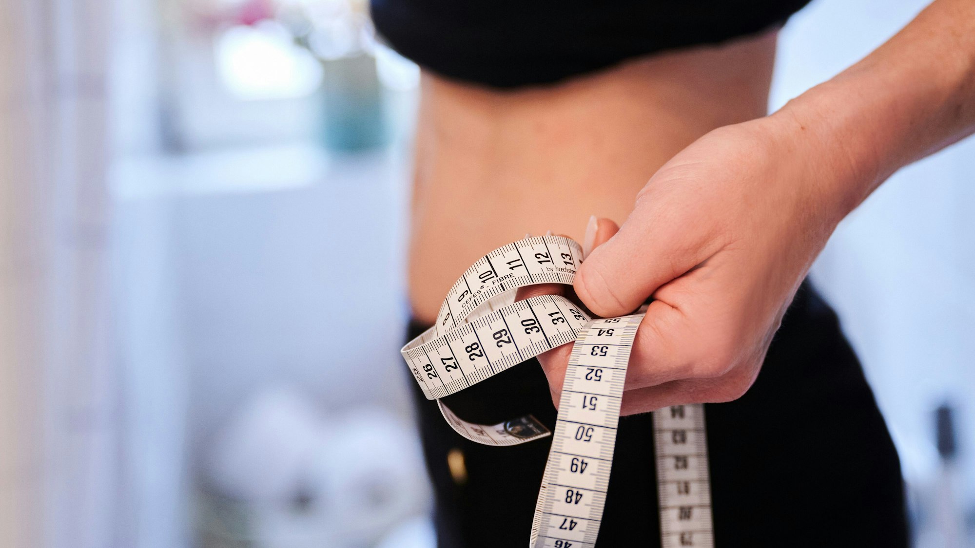 Eine Frau hält ein Maßband an ihren Bauch.