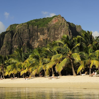 Der Berg Le Morne Brabant ragt hinter den Palmen am Sandstrand hervor.