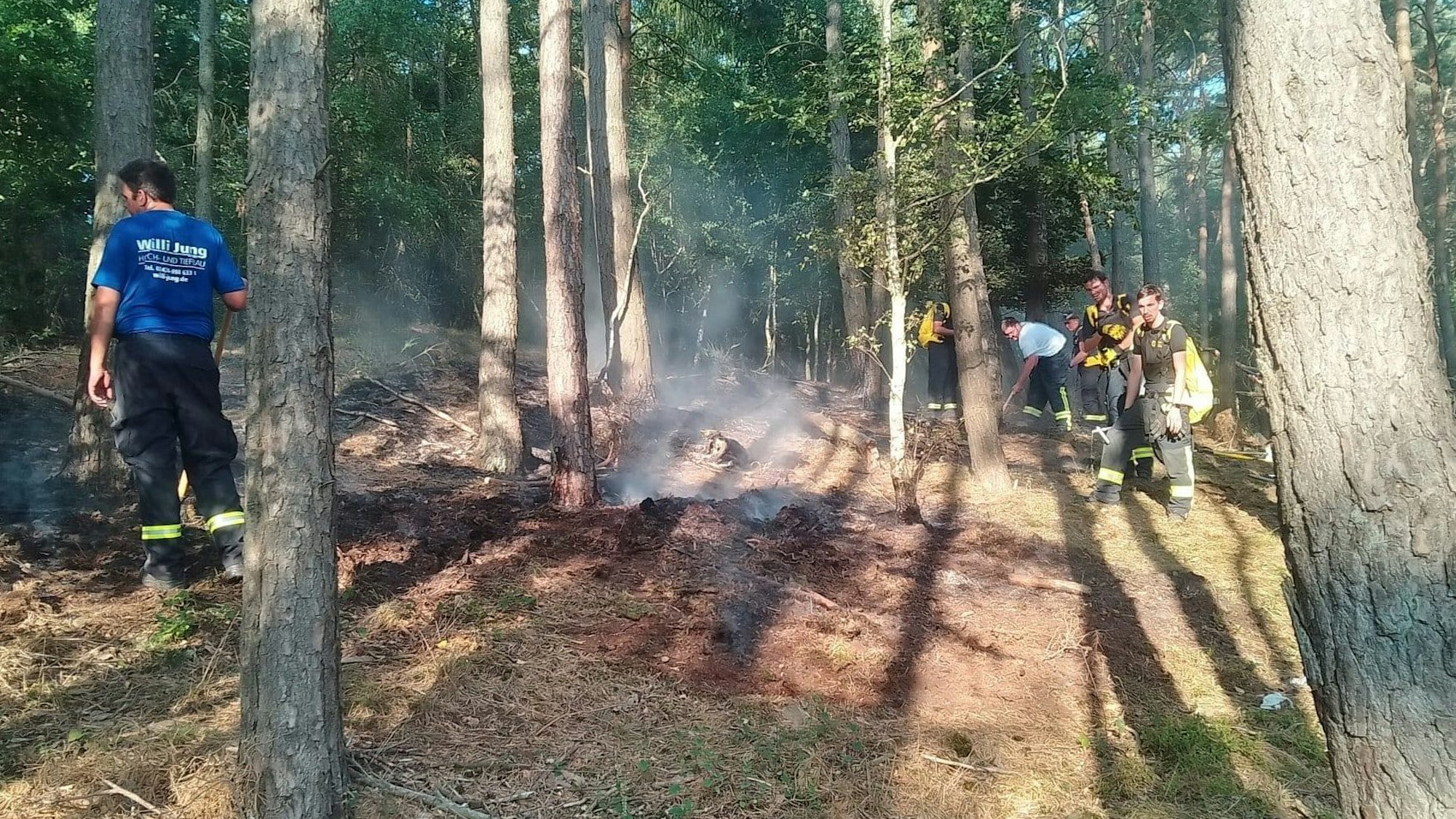 Feuerwehrleute sind zwischen den Bäumen mit Löscharbeiten beschäftigt.