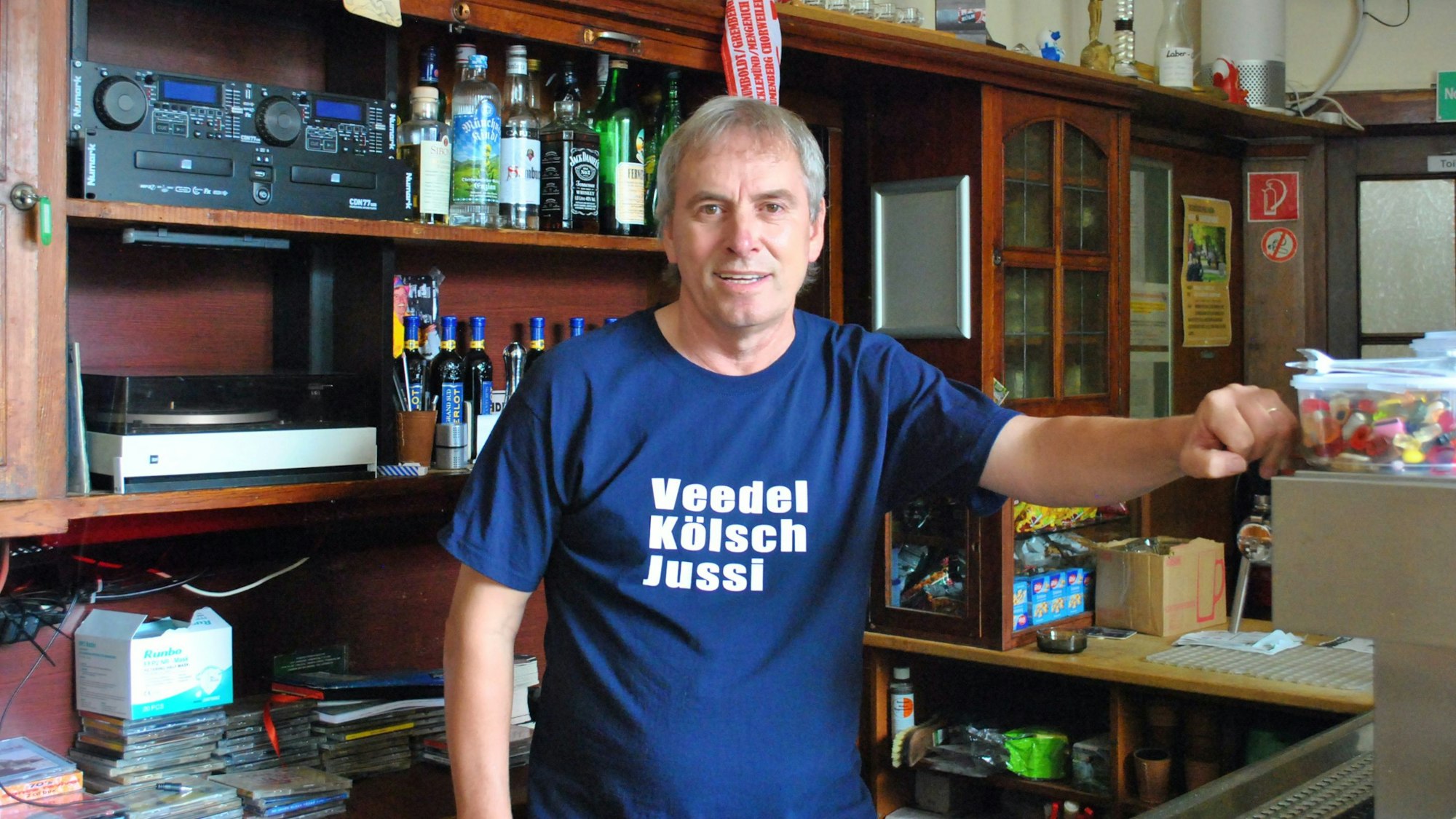 Ein Mann im blauen T-Shirt steht hinter einer Theke.