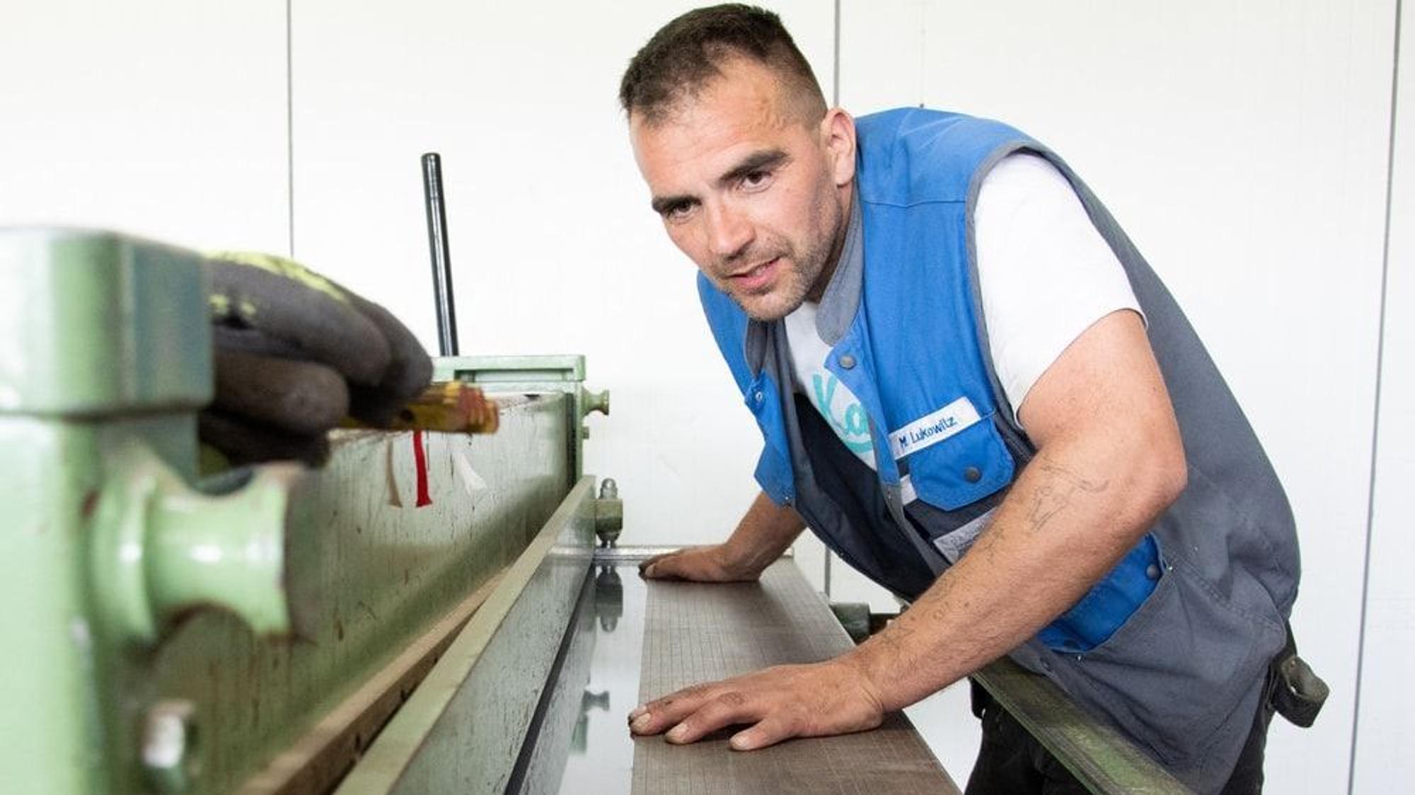 Der Dachdecker steht an einer Maschine.