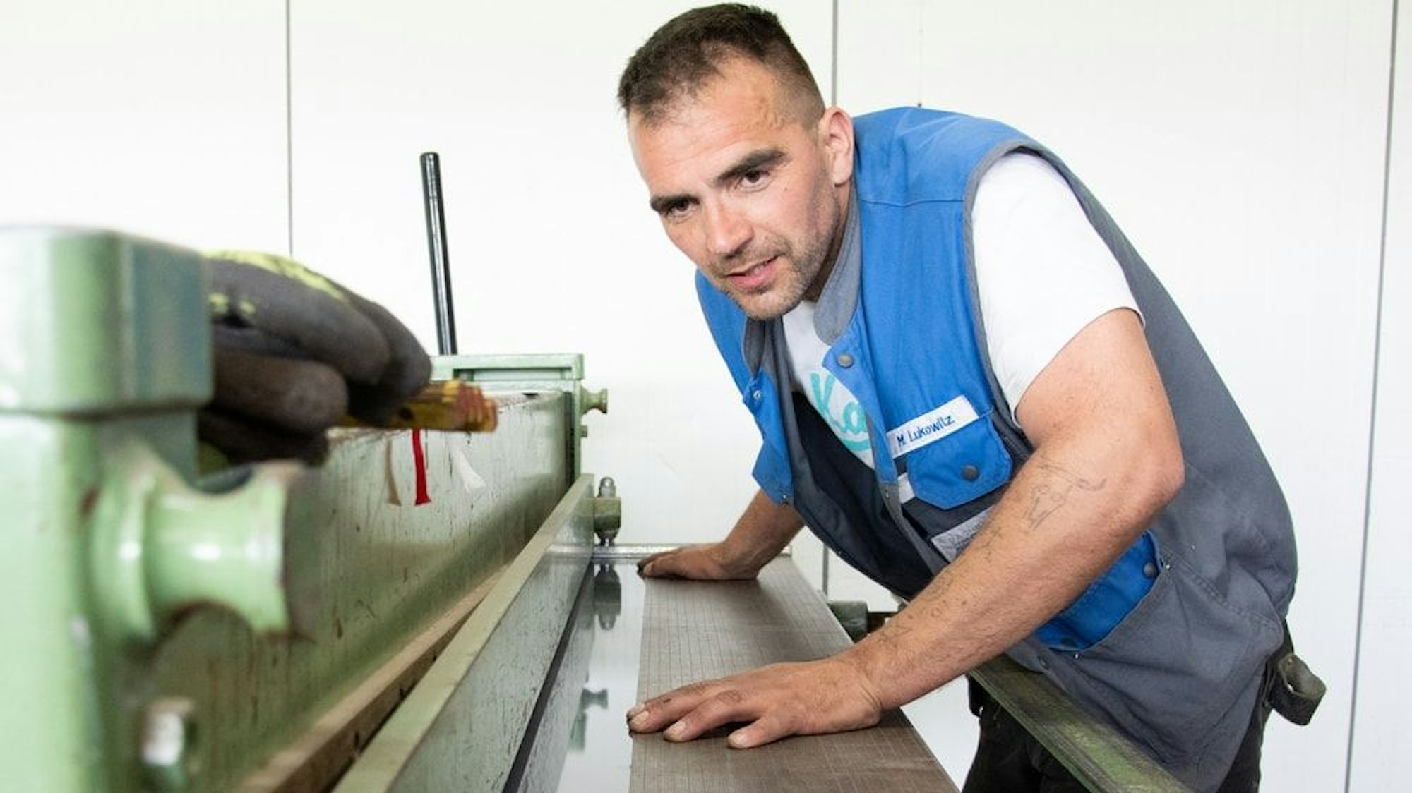 Der Dachdecker steht an einer Maschine.