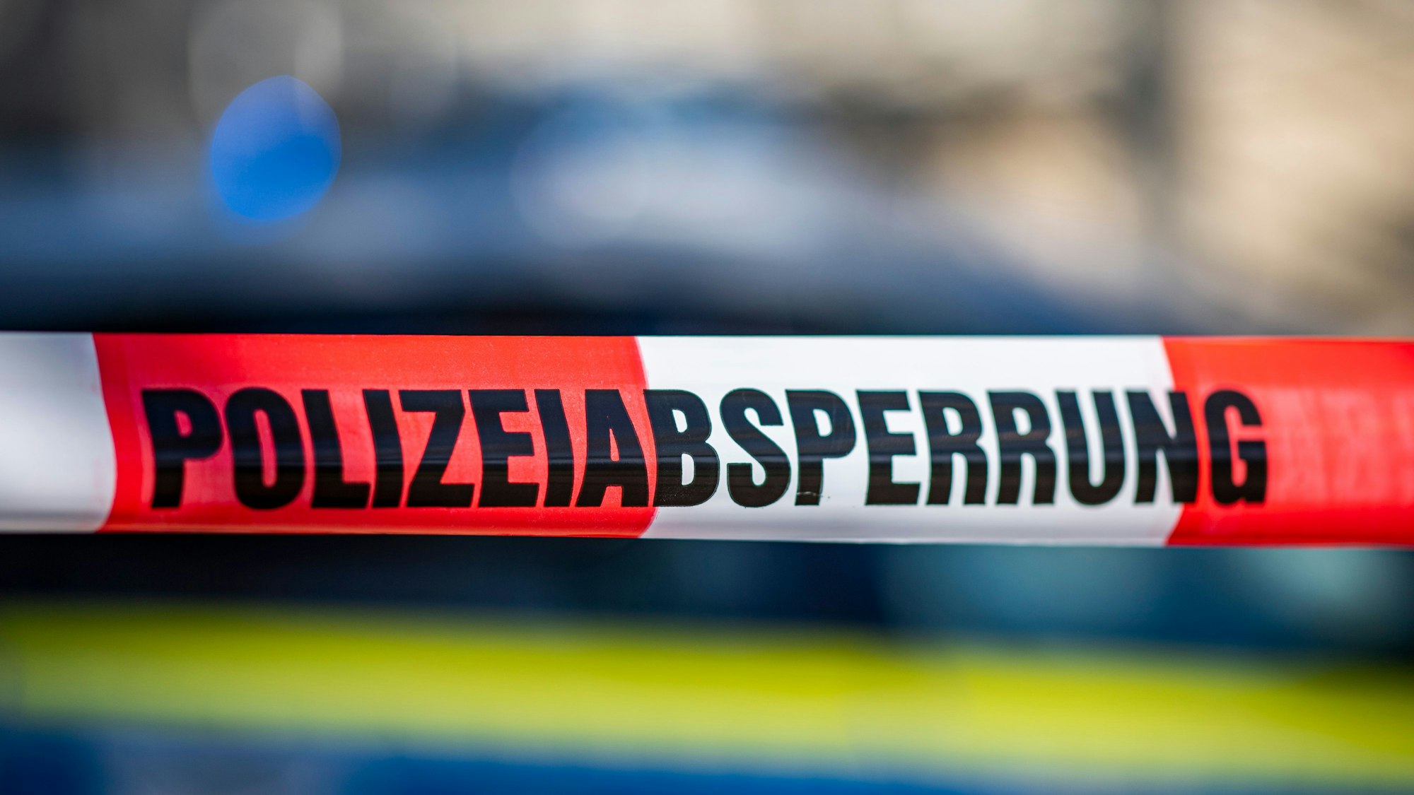 Ein Absperrband mit der Aufschrift „Polizeiabsperrung“ ist vor einem Polizeiwagen aufgespannt.