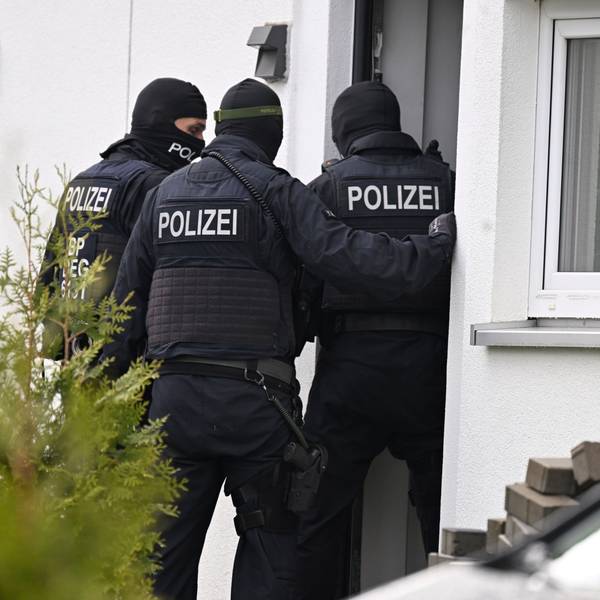 Drei schwarz vermummte Polizisten stehen vor dem Eingang eines weißen Wohnhauses.
