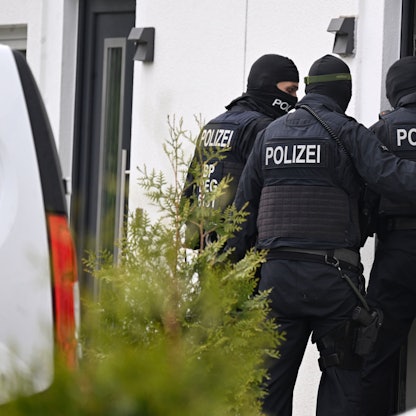 Drei schwarz vermummte Polizisten stehen vor dem Eingang eines weißen Wohnhauses.