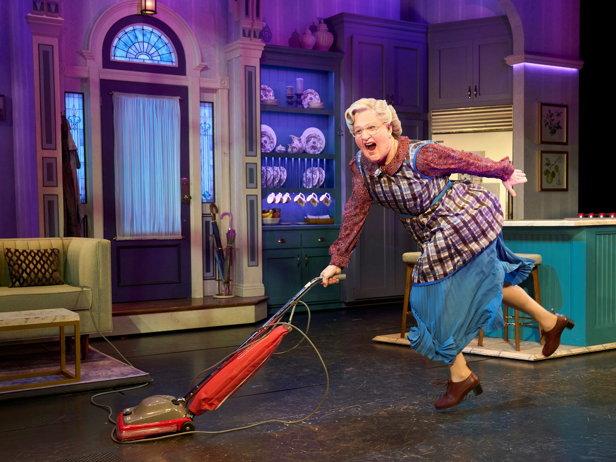 Mrs. Doubtfire tanzt mit einem roten Staubsauger durch eine bunte Bühnenküche.