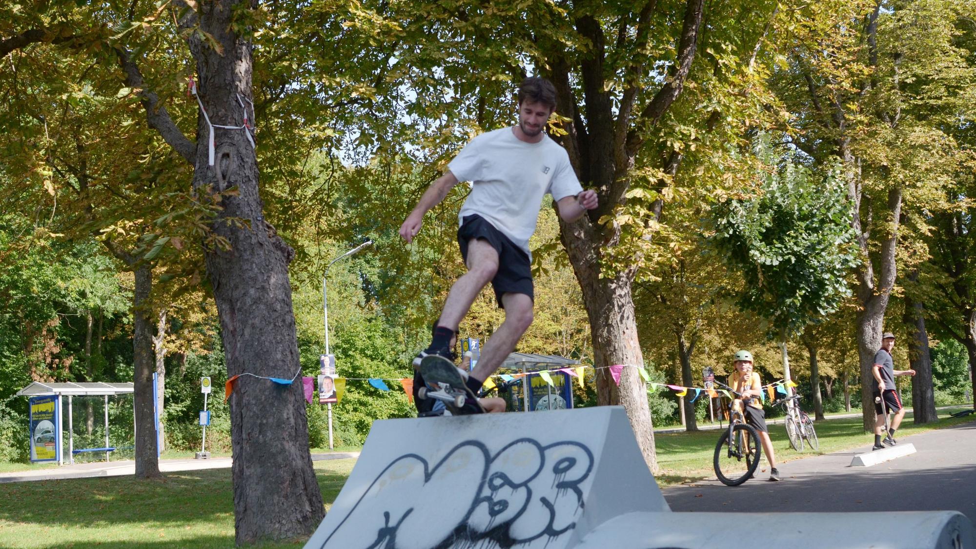 Auf einer Bahn, die von Bäumen gesäumt ist, überwindet ein Skater ein Hindernis.