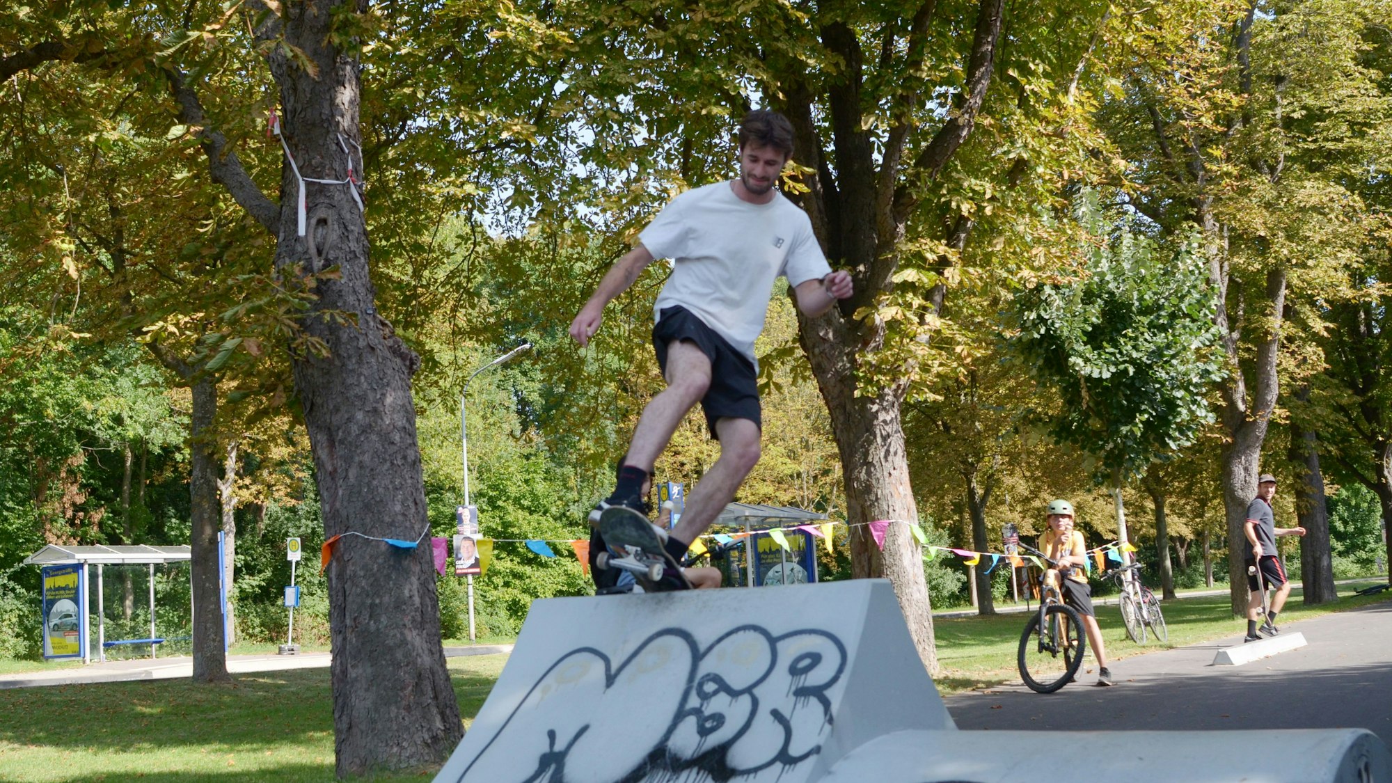 Auf einer Bahn, die von Bäumen gesäumt ist, überwindet ein Skater ein Hindernis.