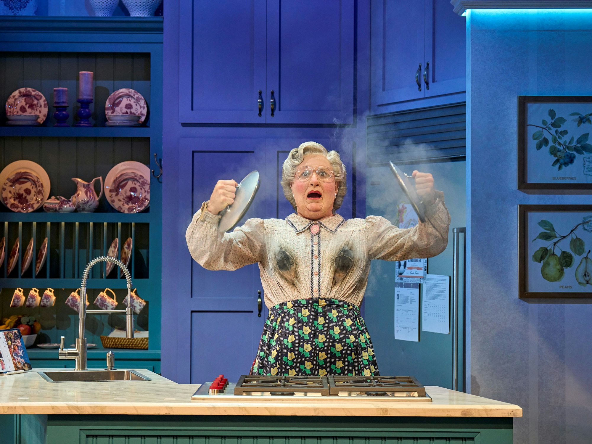 Mrs. Doubtfire steht in einer Küche mit Ruß auf der Kleidung und dampfenden Töpfen.