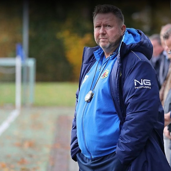 Das Foto zeigt einen Fußballtrainer an der Seitenlinie, die Augen auf das Spiel seiner Elf gerichtet.